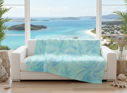 White sofa with a blue and green patterned throw blanket in a room with large windows showing a scenic view of water and land.